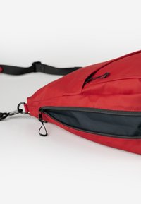 Rote Stoff-Schultertasche mit einem Reißverschlussteil, verfügt über eine glatte Textur, einen verstellbaren Gurt und ein schwarzes Innenfutter.