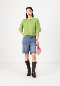 Strikket grønn cardigan med blomsterbroderi, blå jeanshorts, brune knelange støvler og en rosa veske. Enkel, avslappet antrekk.
