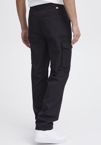 Sorte cargo-bukser med sidelommer, lige ben-design og i bomuldsmateriale. Bæres med hvide sneakers, der viser en minimalistisk stil.