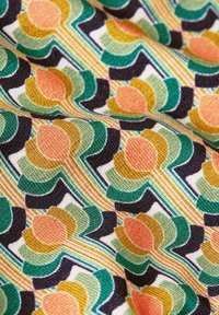 Tekstiili, jossa on elävä geometrinen kuvio vihreän, oranssin, keltaisen ja mustan sävyissä. Kankaassa on tekstuuri ja monimutkaisia yksityiskohtia.