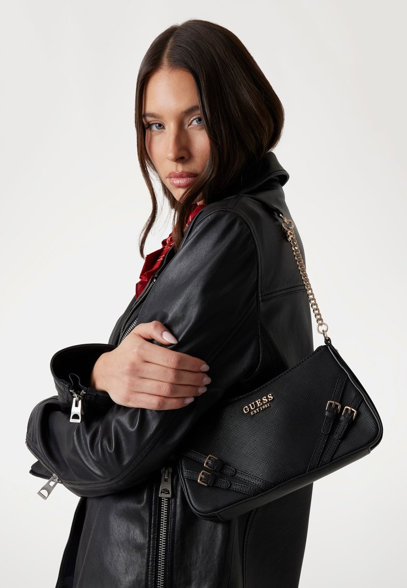 Borsa nera texturizzata con tracolla a catena, caratterizzata da hardware dorato e dettagli di fibbia distintivi. Indossata a stretto contatto con il corpo.
