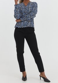 Blommig blus i svart, blått och vitt, med V-ringning och långa ärmar, tillsammans med tajta svarta byxor och svarta spetsiga klackar.