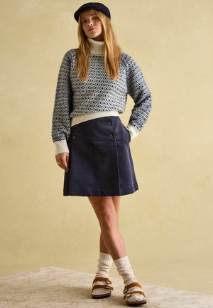 Knit sweater with diamond pattern in navy and cream, paired with a navy corduroy skirt featuring double buttons. Brown sandals and white socks.
