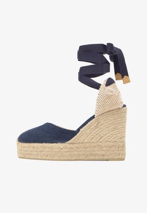 Cuña de esparto azul marino con plataforma de yute trenzado y tiras para atar en el tobillo, con detalle de tacón a cuadros en beige.