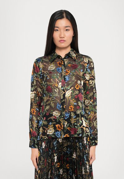 Blouse florale noire transparente avec des fleurs brodées colorées, un col et des fermetures à boutons sur le devant. Manches longues avec poignets.