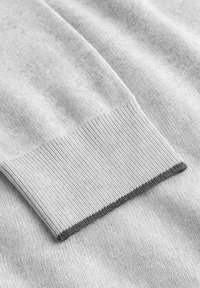 Hellgrauer Strickstoff mit einer gerippten Textur; verfügt über einen kontrastierenden dunkelgrauen Saum am Bündchen. Glatte Oberfläche, Nahaufnahme.