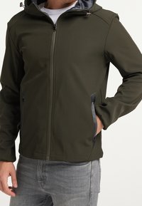 Olivgrön jacka med huva, med en helframsdragkedja, sidofickor och grå detaljer vid kanterna. Slät tygstruktur.