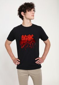 Černé bavlněné tričko s červeným grafickým potiskem skupiny AC/DC, s motivem blesku a siluetami členů kapely.