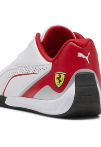 Zapatillas deportivas blancas y rojas con un diseño perforado, que cuentan con una suela de goma negra y un logo de Ferrari amarillo en el lateral.