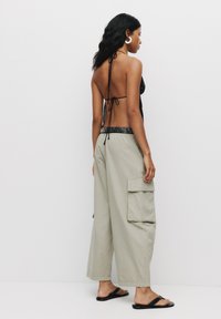 Top nero a fascia con spalline annodate abbinato a pantaloni cargo grigi chiari a gamba larga con due tasche laterali e cintura elastica. Sandali neri.