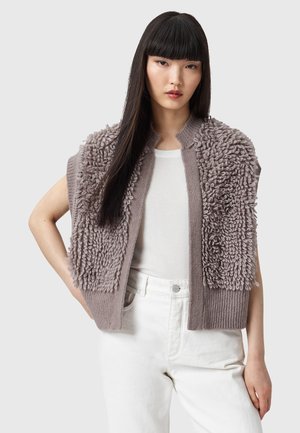 Maglia corta a maniche corte in morbido taupe con sezioni di filato testurizzato e soffice. Orlo a coste e design aperto, abbinata a una maglietta bianca.
