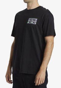 Camiseta de algodón negra de manga corta, con un diseño colorido de olas en un parche cuadrado en el frente y un corte relajado.
