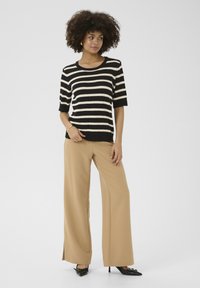 Pull en tricot rayé noir et beige à manches courtes, associé à un pantalon large beige et des chaussures à bout pointu noires.