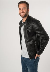 Schwarze Leder-Motorradjacke mit Reißverschluss und Druckknopfkragen, ausgestattet mit strukturiertem Material und einer seitlichen Taschenkennung.