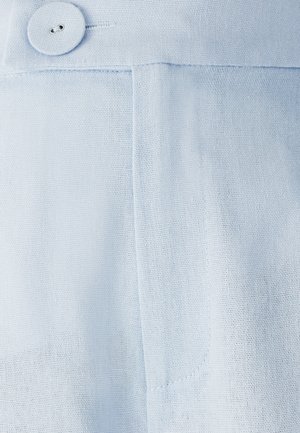 Blízko k modré látce s texturovanou vazbou, kulatým knoflíkem a prošívanými detaily kapsy. Hladký a měkký vzhled.