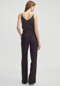 Bruine high-waisted broek gecombineerd met een gestructureerde donkere top met dunne bandjes. De outfit is stijlvol, met een slim-fit en eigentijds ontwerp.