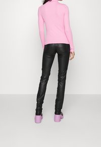 Rosa långärmad polotröja som sitter snuggt, i kombination med svarta skinnbyxor och lavendelfärgade klackskor, sedd från baksidan.