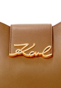 Brown faux leather bag with a gold-tone "Karl" signature logo. Smooth texture with stitched edges and a flap closure.