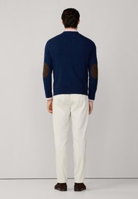 Suéter navy con parches marrones en los codos, diseño ajustado, punto texturizado. Combinado con pantalones crema, completado con mocasines oscuros.