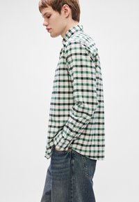 Grønt og hvitt rutete skjorte med lange ermer, knapp-ned krage og en avslappet passform, parret med mørkeblå jeans.