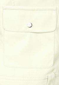 Vêtement en simili cuir blanc avec une poche à rabat, un accent de bouton-pression argenté, des couture décoratives et une texture lisse.