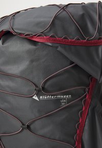 Black nylon backpack with maroon accents, featuring a drawstring closure, adjustable straps, and a logo label. Textured, durable material.