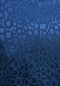 Głęboki niebieski materiał z textured wzorem o różnorodnych okrągłych kształtach, z gładkimi, wypukłymi elementami dla dodatkowego zainteresowania wizualnego.