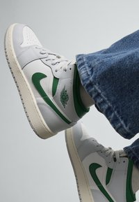 Sneaker bianche in pelle con dettagli verdi, punta perforata e suola in gomma testurizzata, abbinate a jeans in denim.