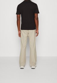 Svart kortärmad t-shirt i kombination med beiga rutiga vida byxor. Byxorna har ett rutigt mönster och en avslappnad passform; skorna är vita.