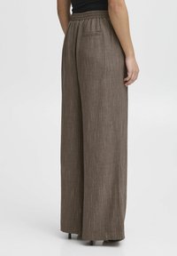 Vida byxorna i strukturerat brunt tyg med subtila vertikala ränder. Har en elastisk midja och en bakfickdetalj.
