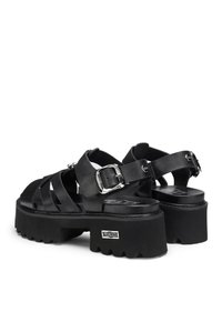 Sandali platform neri con larghe cinghie incrociate, dettagli con fibbie argentate e suola testurizzata per aderenza e stabilità.
