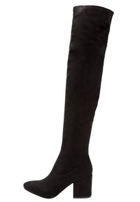 Bottes noires au-dessus du genou en daim doux. Embout pointu et talon épais. Texture lisse avec une coupe ajustée le long de la jambe.