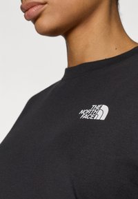 Μαύρο βαμβακερό t-shirt με στρογγυλή λαιμόκοψη, με μικρό λευκό λογότυπο στο αριστερό στήθος που γράφει "THE NORTH FACE." Ομαλή υφή.