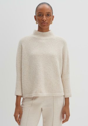 Light beige, textured sweater with a high collar and three-quarter sleeves, paired with light beige pants. Simple and cozy design.