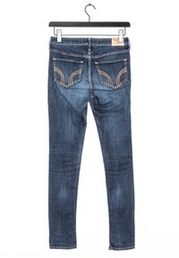 Dark blue skinny jeans with visible stitching, two back pockets featuring curved details, and a smooth denim texture.