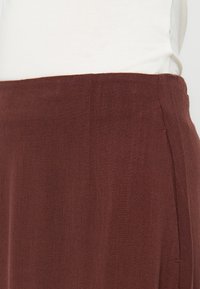 Gros plan sur la taille d'une jupe en lin marron associée à un haut blanc, montrant la texture du tissu et les détails de la couture latérale.