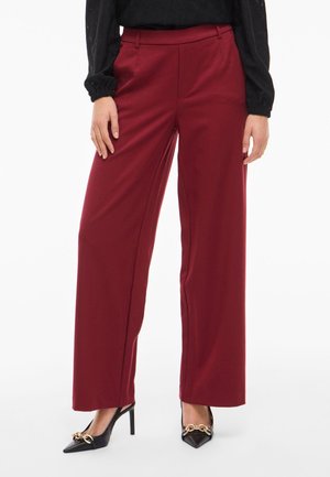 Wijduitlopende broek van bordeauxstof, met een gladde textuur en riemlussen. Gecombineerd met zwarte puntige hakken en gouden hardwareaccenten.