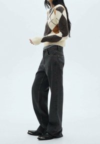 Maglione lavorato a maglia con motivo a diamante in marrone, crema e arancione; abbinato a jeans a gamba larga grigio scuro e scarpe nere.