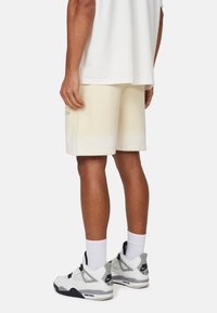Pantaloni shorts color crema con una texture liscia, caratterizzati da una vestibilità comoda. Abbinati a sneaker bianche e calzini alla caviglia. Design semplice.