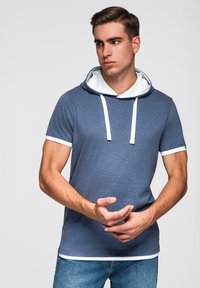 Kratší tričko s kapucí v námořnické modré barvě z bavlny s bílými akcenty. Má kontrastní bílou podšívku kapuce a lemování rukávů.