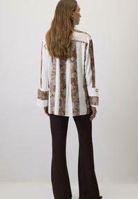 Košulja dugih rukava s smešnim čipkastim uzorcima i belim prugama, s dugmetom na manžetama, u kombinaciji s crnim širom hlačama.