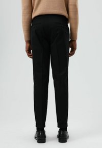 Zwarte op maat gemaakte broek met smalle pasvorm, platte voorkant, twee achterzakken en opgerolde boorden, gedragen met een beige gebreide trui.