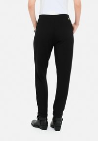 Sorte jogger-style bukser lavet af blødt stof, med en tætsiddende ankel, sidelommer og en lille guld logo-accents på linningen.