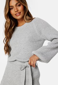 Maglione grigio a coste con maniche lunghe, scollo rotondo e dettaglio in vita con cintura. Texture morbida e vestibilità comoda.
