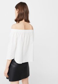 Weiße schulterfreie Bluse mit elastischem Ausschnitt und Dreiviertelärmlen, kombiniert mit einem schwarzen Minirock, mit Fokus auf einem minimalistischen Design.