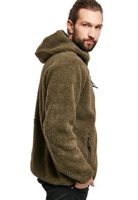 Veste en polaire vert olive douce avec capuche, dotée d'un zip sur le devant et de cordons de serrage ajustables. Texture douce avec une coupe décontractée.