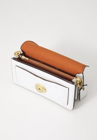Witte leren handtas met een gladde textuur, gouden details en een bruine voering; voorzien van een ritssluiting en een decoratieve haak.