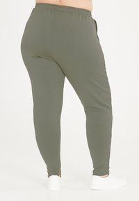 Olivengrønne leggings lavet af blødt, strækbart stof med et tætsiddende design. Elastisk talje og nedre kant på anklerne. Kombinationen er med hvide sneakers.