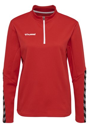 Pullover de sport rouge avec un col à moitié zippé, présentant un tissu texturé et des accents en chevron noir et blanc sur les manches. Logo Hummel visible.