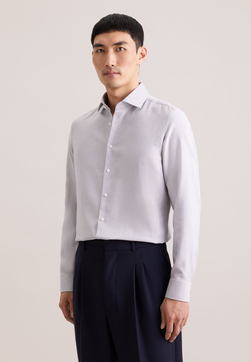 Chemise gris clair à motif avec col boutonné, manches longues et coupe décontractée, associée à un pantalon tailleur bleu marine.